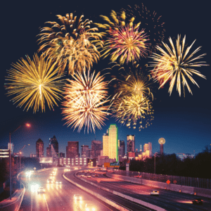 Nighttime view of the Dallas skyline with vibrant fireworks exploding in the sky above a busy highway, symbolizing celebration and energy in the city.