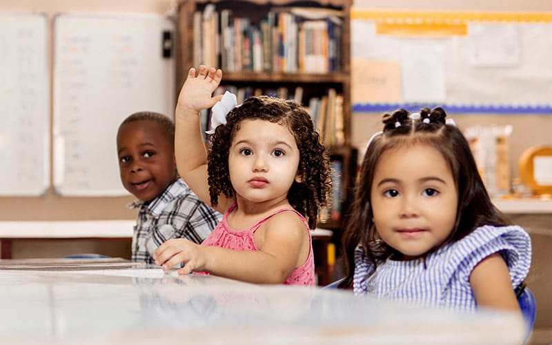 3 small children in class one with her hand raised