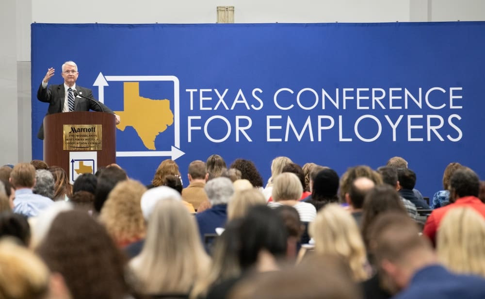 A speaker at the podium addresses a large audience at the Texas Conference for Employers.